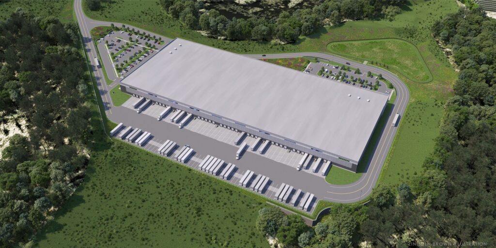 Aerial view of a large warehouse with multiple loading docks. Numerous trucks are parked in designated areas. Surrounding the building are green spaces and trees, with a parking lot on one side. Curved roads lead to and from the facility.