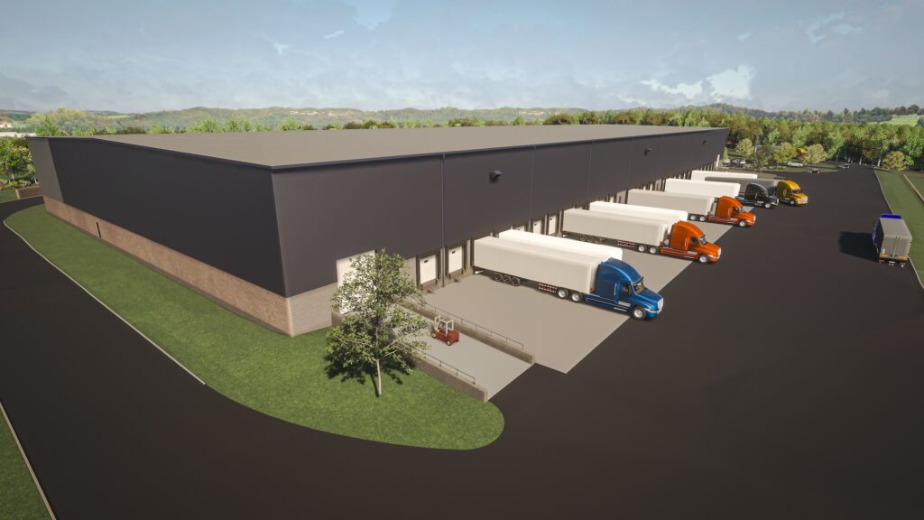 Aerial view of a large, dark-gray warehouse with multiple loading bays. Several trucks, including blue, orange, and white ones, are parked at the bays. The warehouse is surrounded by greenery under a partly cloudy sky.