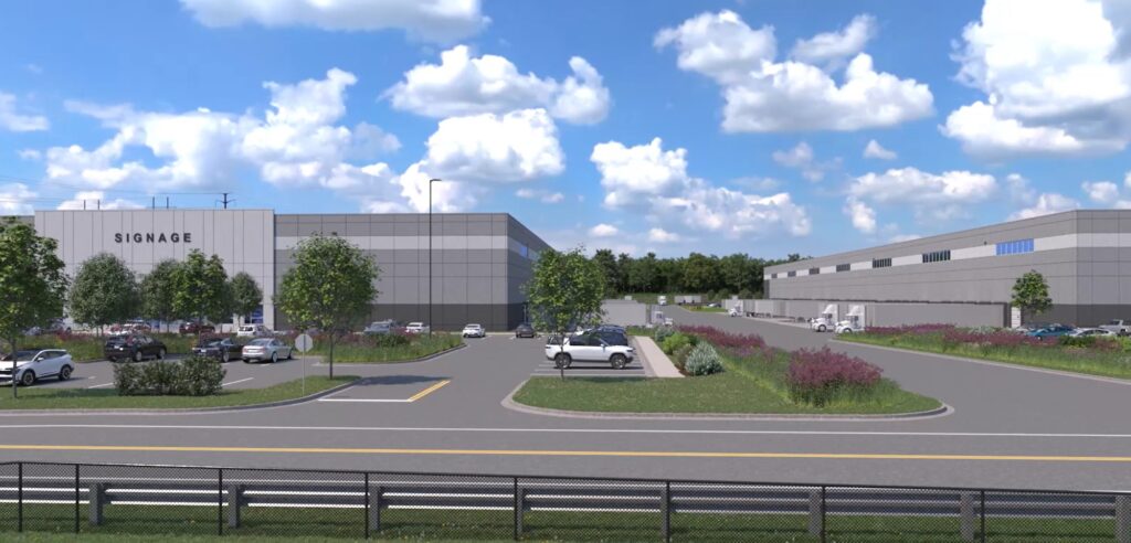 Industrial buildings with SIGNAGE on one, surrounded by greenery and parked cars. A clear sky with scattered clouds overhead. The scene includes roads and parking spaces with trucks and cars.