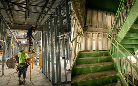 Construction scene with two workers in hard hats and safety gear assembling metal frames in a building interior. A green-painted metal staircase is visible to the right, situated near unfinished walls.