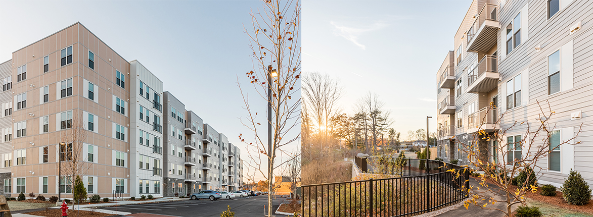 Wide-angle view of modern apartment buildings with beige and white exteriors. The scene is under a clear sky with a setting sun. Bare trees and a few small shrubs are visible, alongside a black railing and a red fire hydrant.