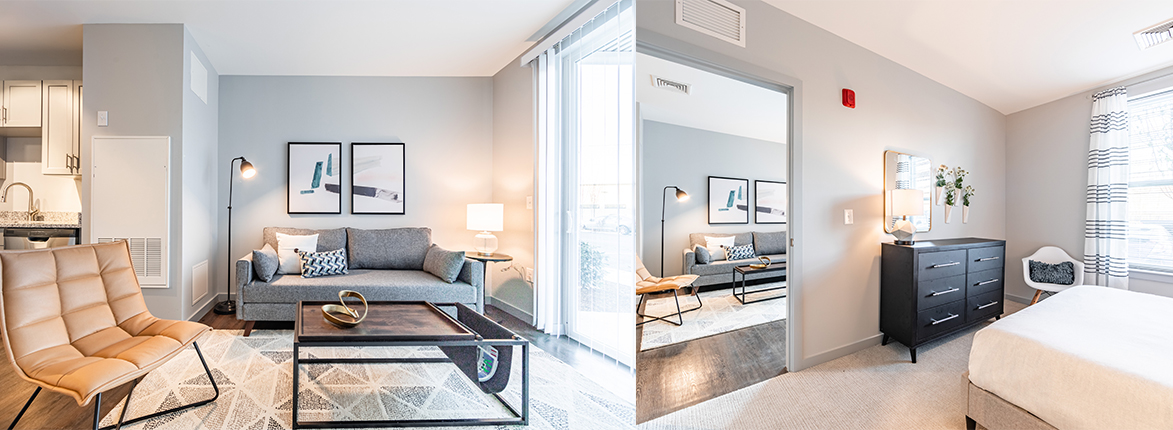 Modern, well-lit apartment featuring a living area with a gray sofa, two brown chairs, and a black coffee table. A kitchen is visible in the background. Adjacent is a bedroom with a bed, dresser, and mirror, decorated in neutral tones.